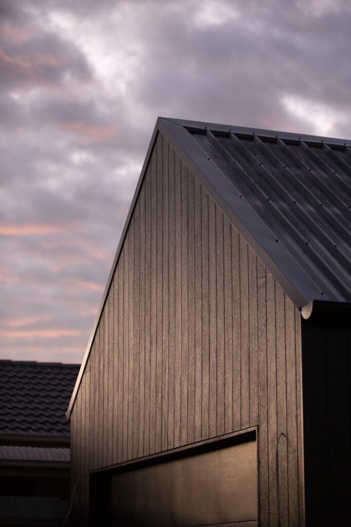 A modern house with a sleek metal roof stands against a dramatic cloudy sky.